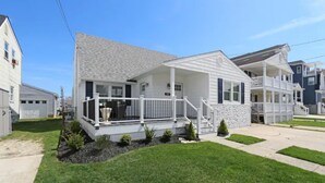 A two-story residential house with a front porch, a small garden, and a clear blue sky.