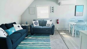 A cozy living room with a dark blue sofa, a matching armchair, and a patterned rug. A small side table with a decorative item is visible.