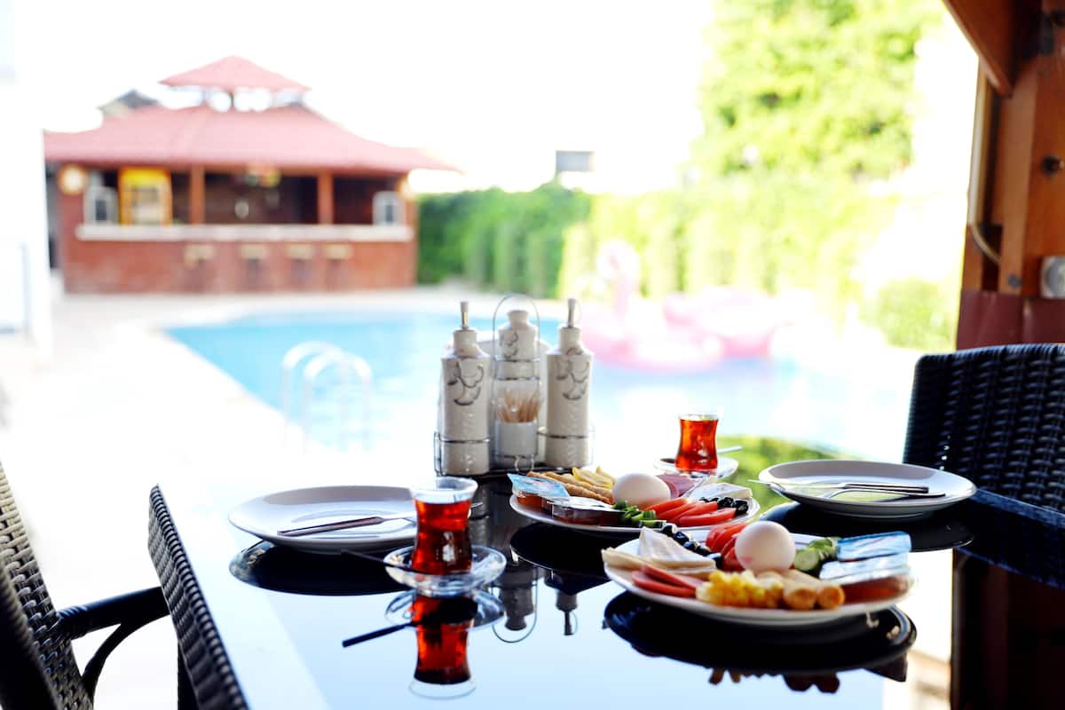 A dining table with plates of food, glasses, and a pool in the background.