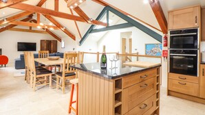 A spacious kitchen with wooden cabinets, a double oven, and a dining area with a wooden table and chairs. - Polurrian House (Helston)