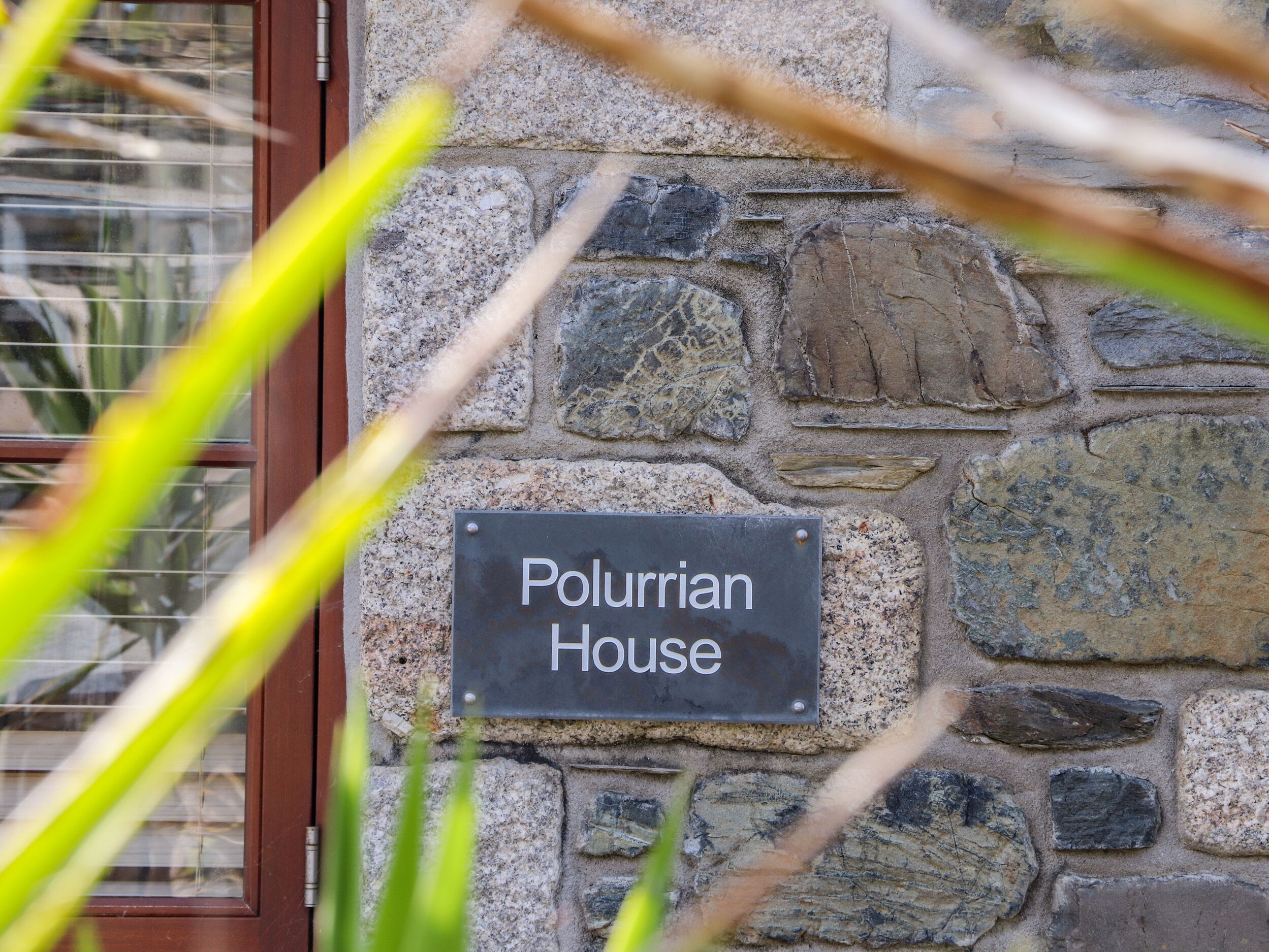 A stone wall with a sign reading "Polurrian House".