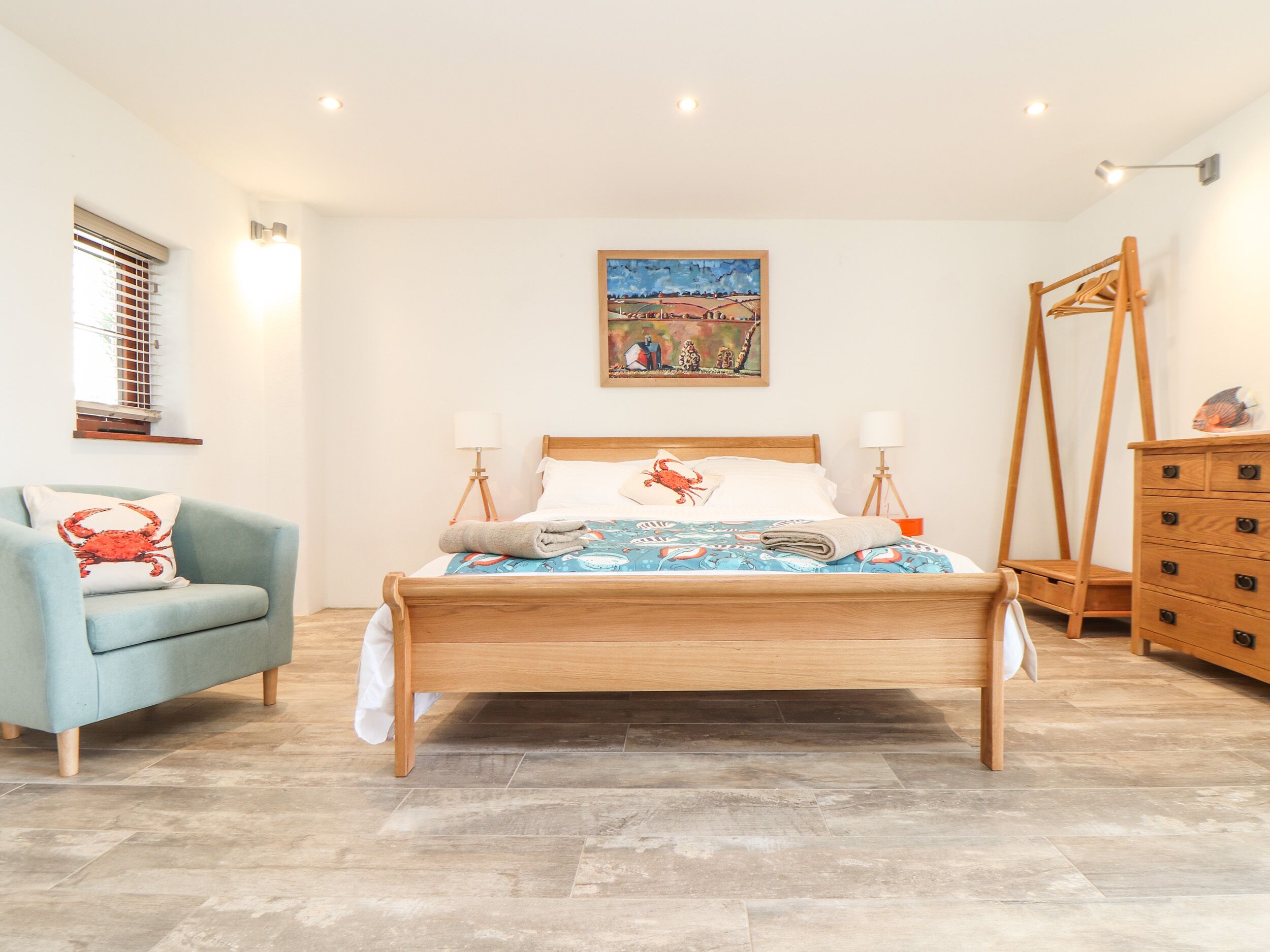 Un dormitorio ordenado con una cama de madera, un sillón azul y un aparador de madera.