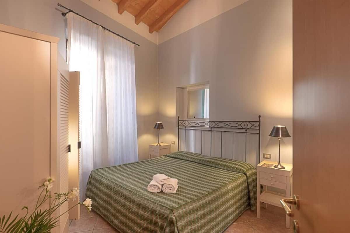 A bedroom with a bed, two bedside tables, a window, and a door.