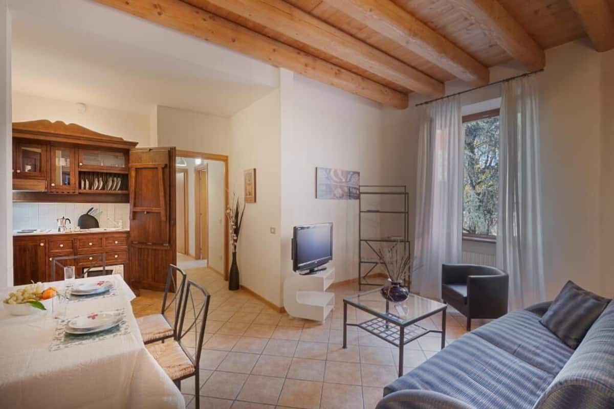 A living room with a sofa, a dining table set with plates, a TV, and a kitchen area with wooden cabinets.