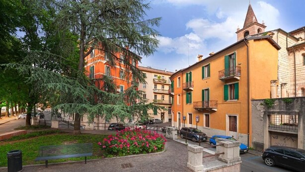 A courtyard with a bench, a flower bed, and parked cars. - San Lorenzo (Verona)