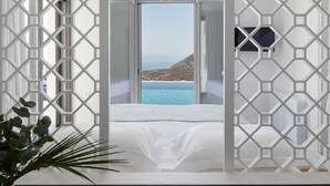 A room with a large window offering a view of the sea and a mountainous landscape. - Kamini White I Villa (Santorini)