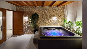 A spa area with a stone wall, wooden ceiling beams, a hot tub, and potted plants. - Kamini White I Villa (Santorini)