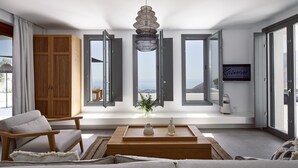 A modern living room with a sofa, a wooden coffee table, and a view of the sea through large windows. - Kamini White I Villa (Santorini)