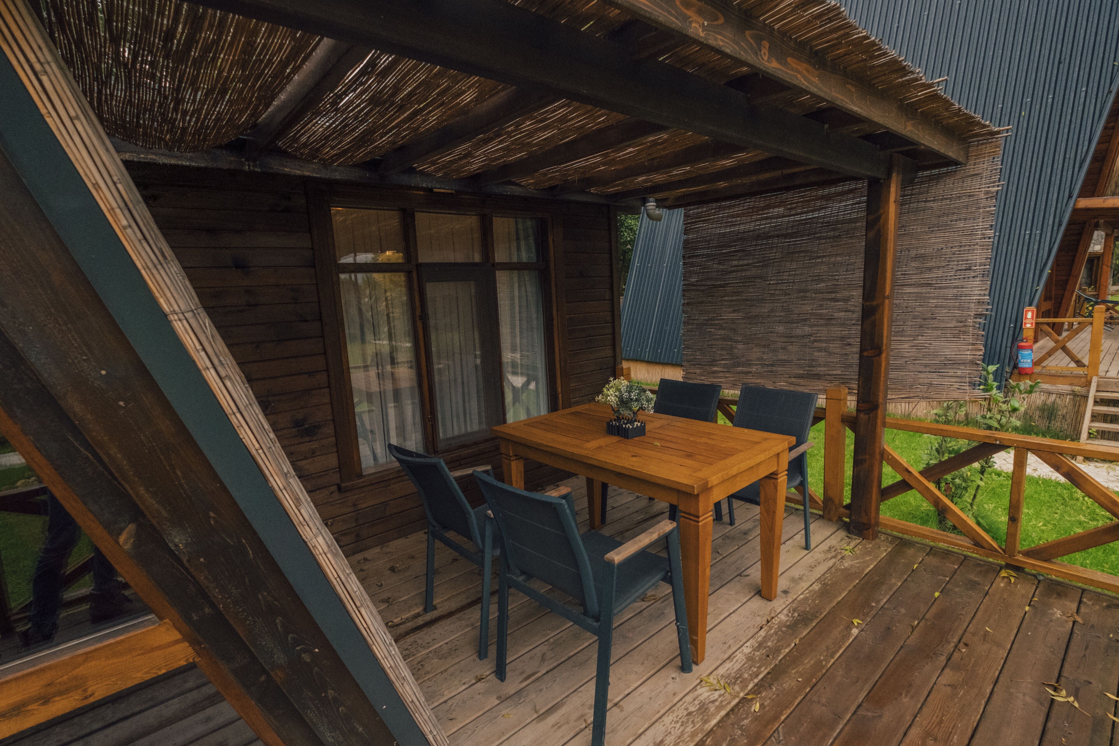 A wooden deck with a table and chairs, a covered area with a thatched roof, and a view of a garden.