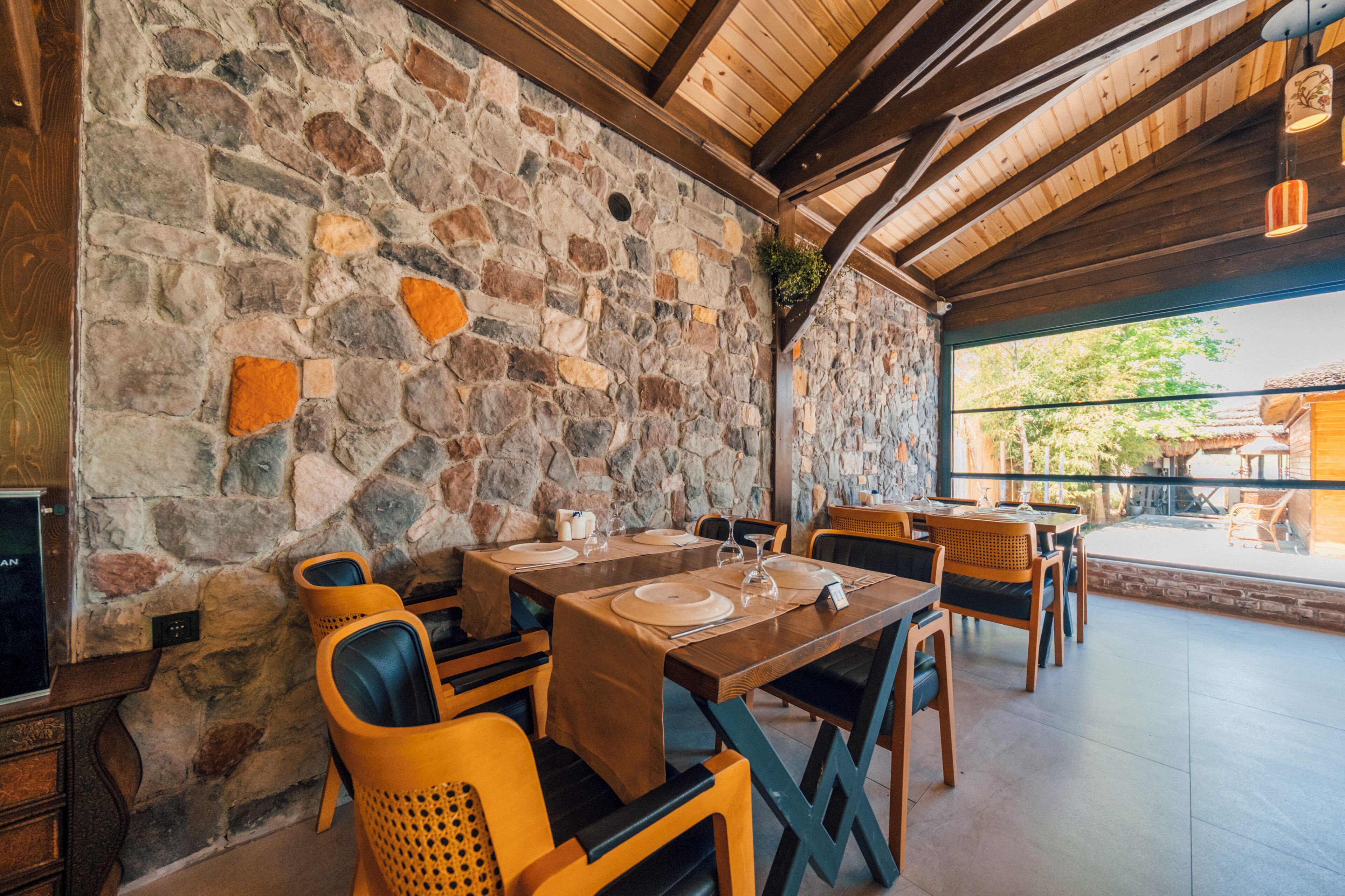 A stone wall, wooden ceiling beams, and a dining area with tables and chairs.