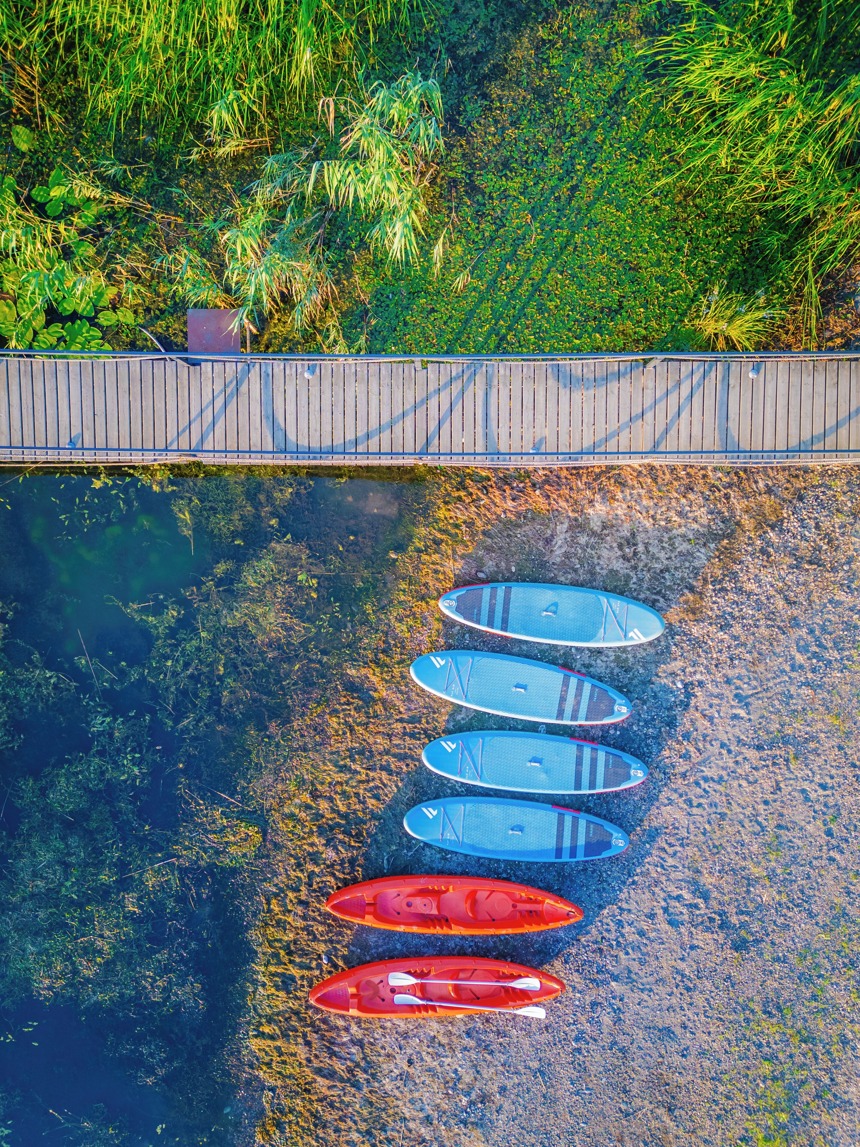 A row of kayaks lined up on a pebbled shore next to a wooden dock.