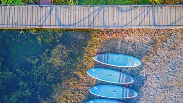 A row of kayaks lined up on a pebbled shore next to a wooden dock.