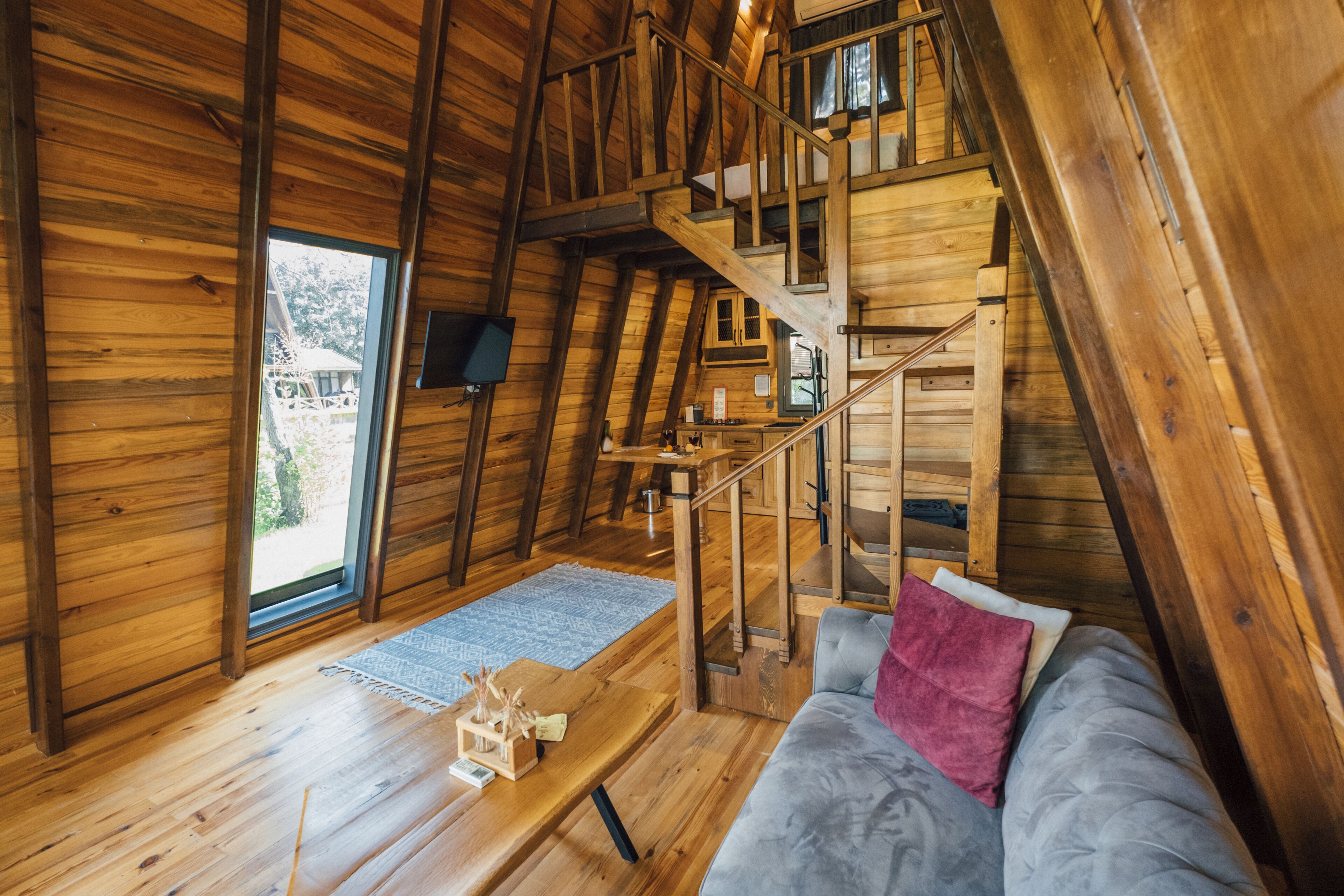 A wooden interior with a staircase leading to an upper level, a sofa with a pink pillow, and a wooden table with a small decorative item.