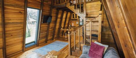 A wooden interior with a staircase leading to an upper level, a sofa with a pink pillow, and a wooden table with a small decorative item.