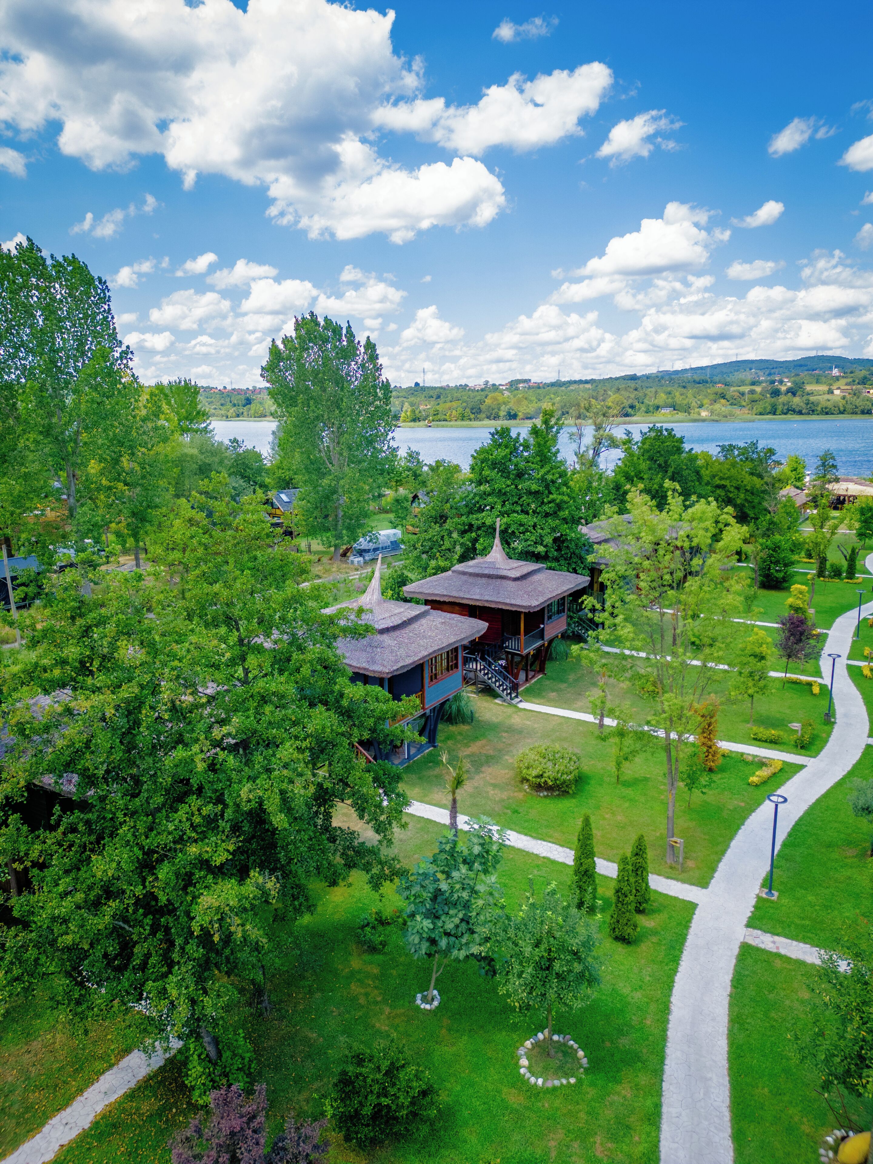 A lakeside property with a gazebo, a thatched-roof building, and a paved walkway.