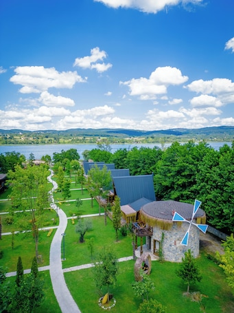 A resort with a thatched-roof structure, a windmill, and a pathway leading to a lake.