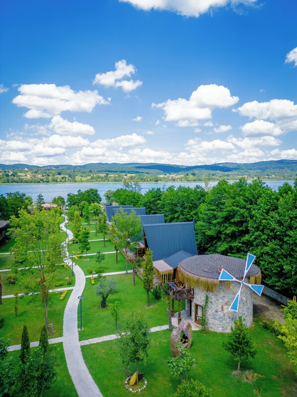 Un resort con una estructura de techo de paja, un molino y un sendero que lleva a un lago.