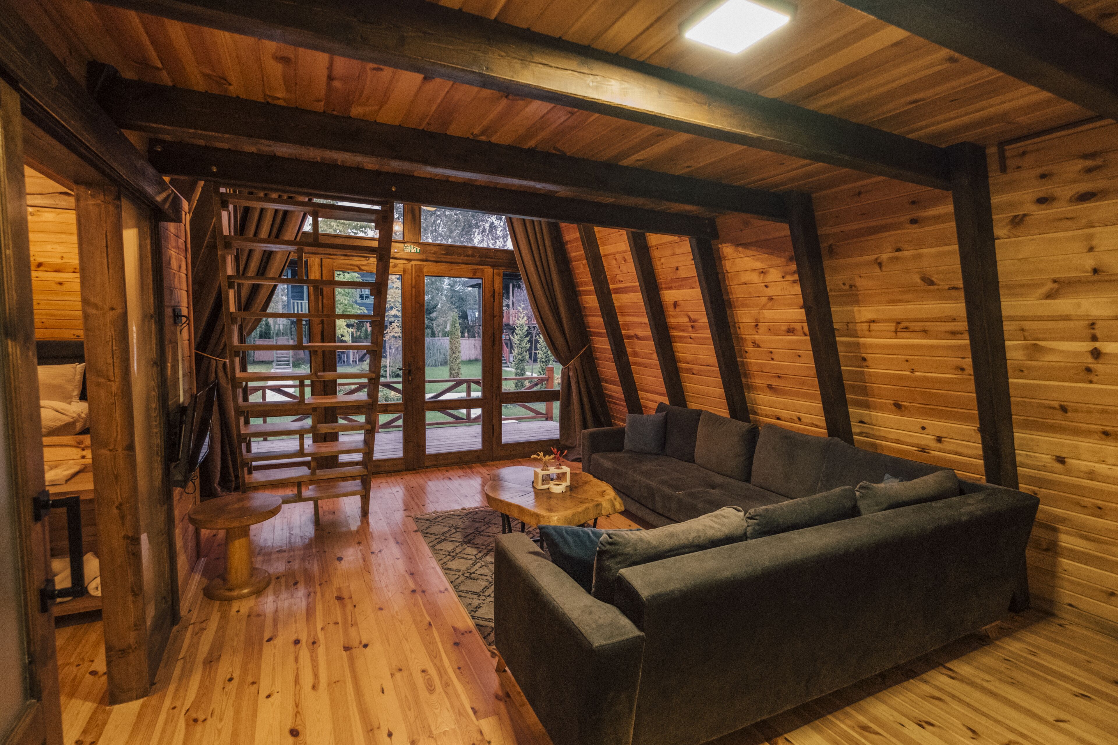 A cozy wooden interior with a sofa, a small table, and a view of the outdoors through large windows.