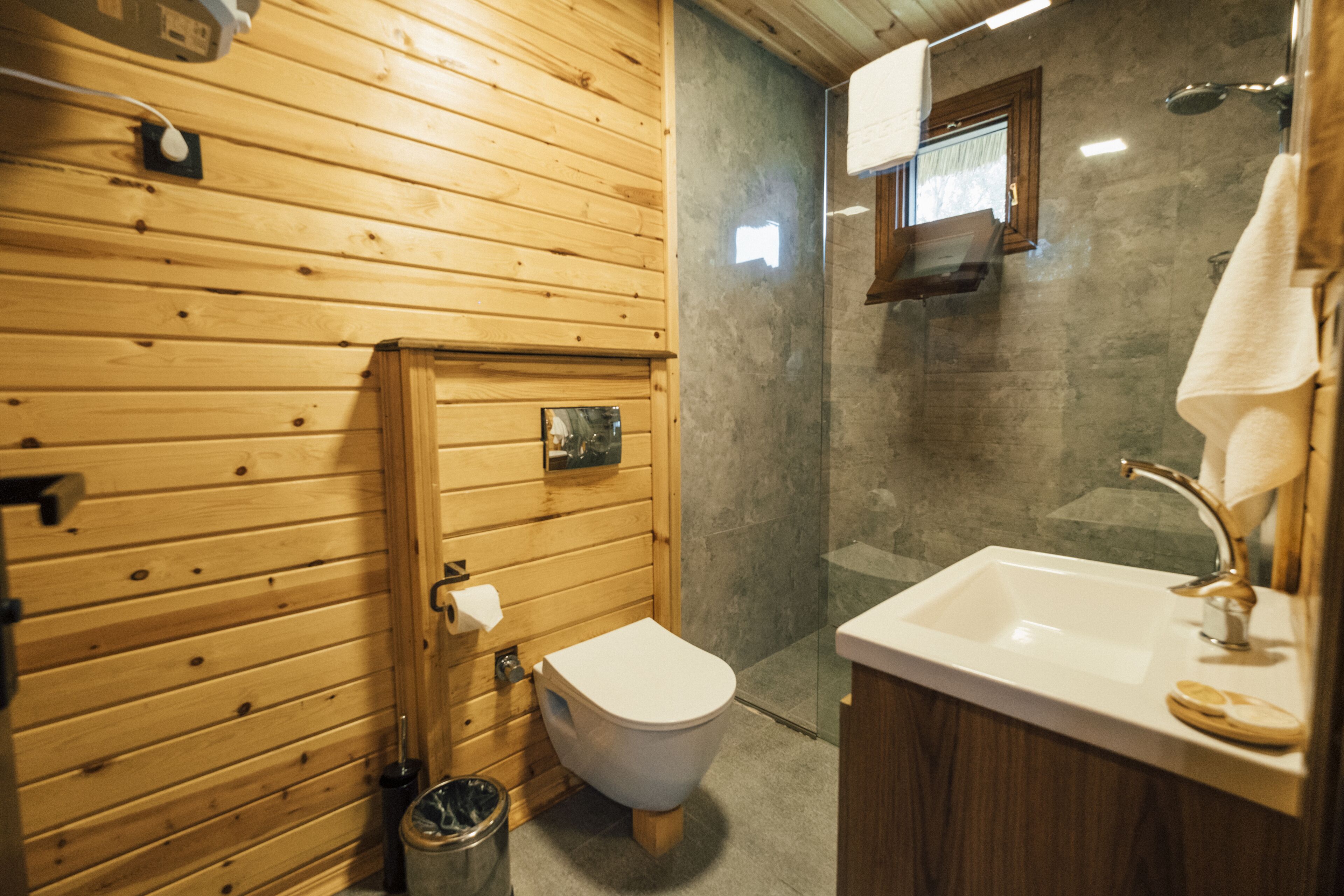 A wooden-paneled bathroom with a toilet, sink, and glass-enclosed shower.