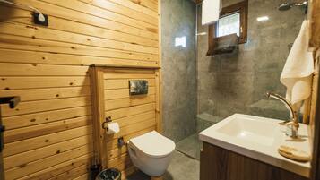 A wooden-paneled bathroom with a toilet, sink, and glass-enclosed shower.