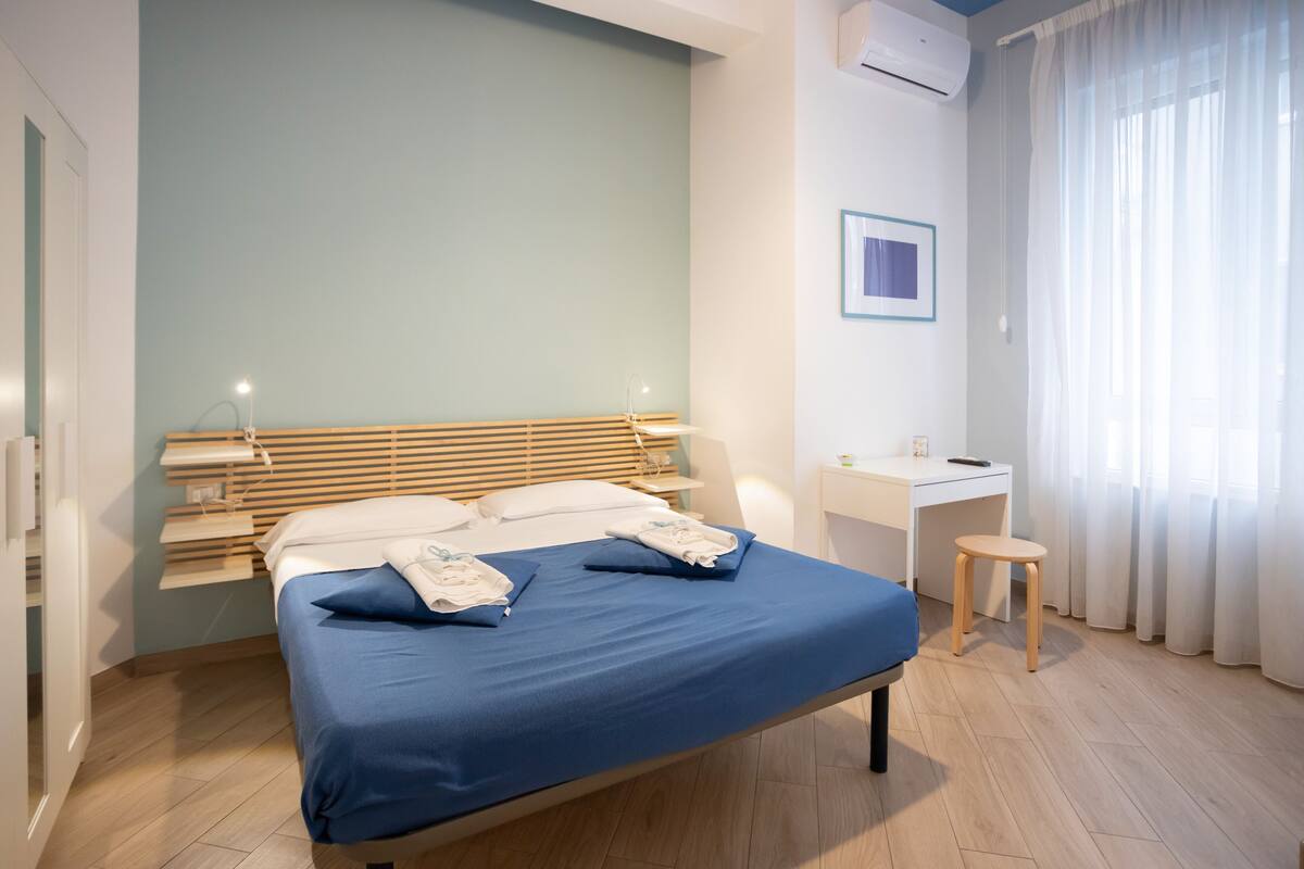 A modern bedroom with a bed, bedside table, desk, and chair.