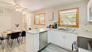 Une cuisine moderne avec des meubles blancs, un coin repas comprenant une table et des chaises, et un ventilateur de plafond.