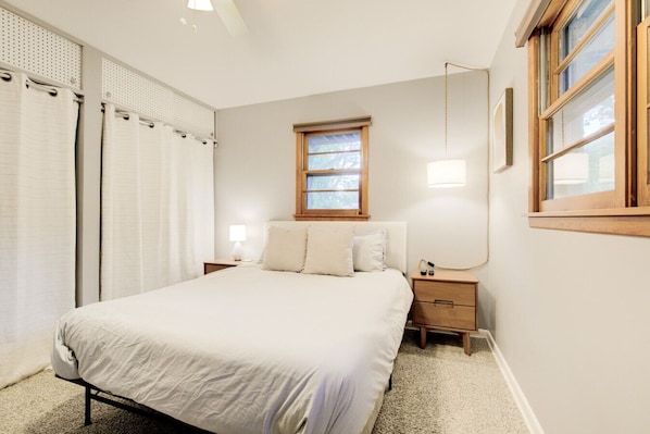 A bedroom with a bed, two bedside tables, a window, and a wall-mounted lamp.