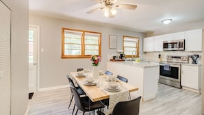 Une cuisine moderne avec des meubles blancs, un four à micro-ondes, un four traditionnel et un coin repas comprenant une table et des chaises en bois.