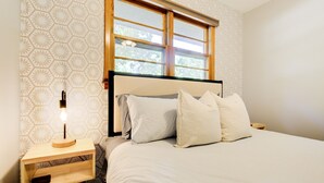 Une chambre à coucher avec un lit, des oreillers, une table de chevet avec une lampe et une fenêtre.