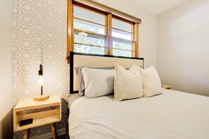 A bedroom with a bed, pillows, a bedside table with a lamp, and a window. - Stadium Station | MHK - Walk to Sports Complex! (Manhattan)
