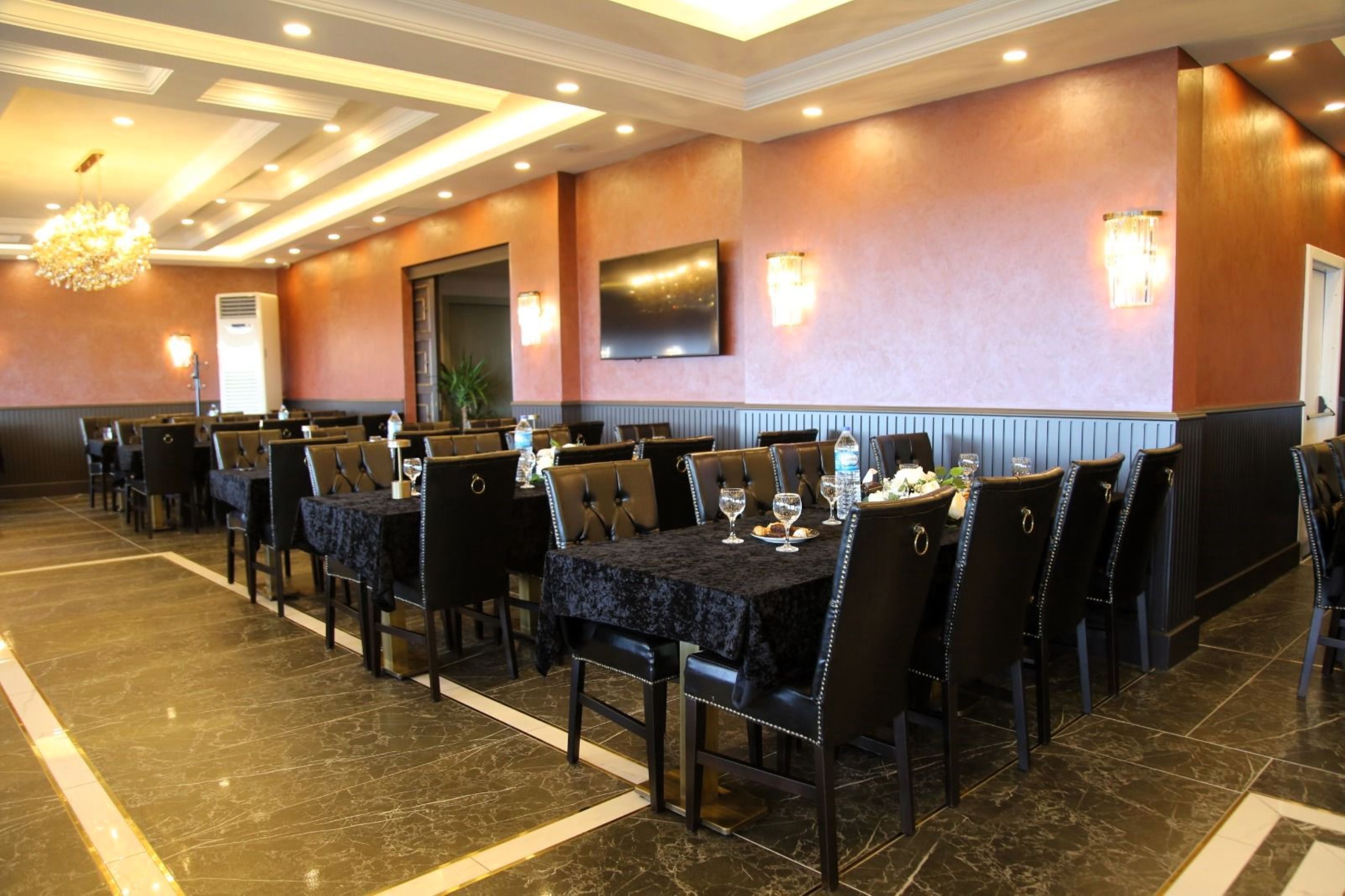 A hotel dining area with multiple tables and chairs, a chandelier, and wall-mounted lighting.