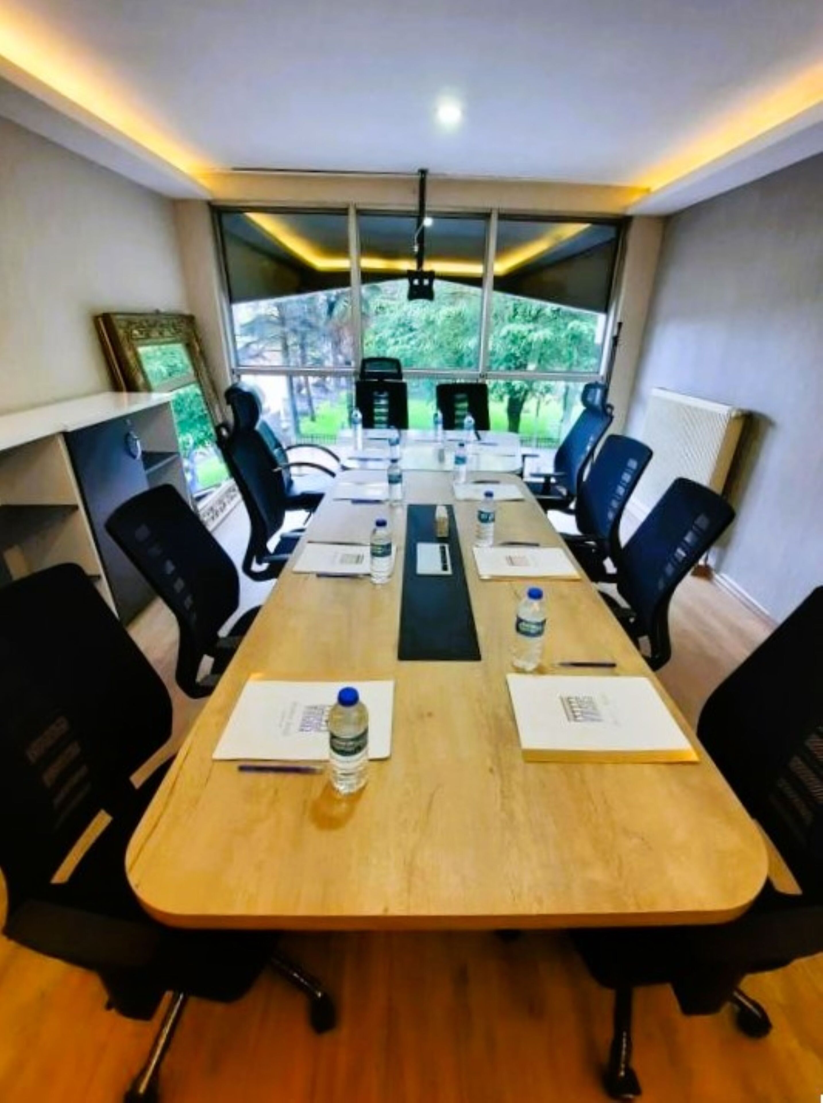 Ett konferensrum med ett långt bord, svarta stolar och utsikt över grönområden utanför.
