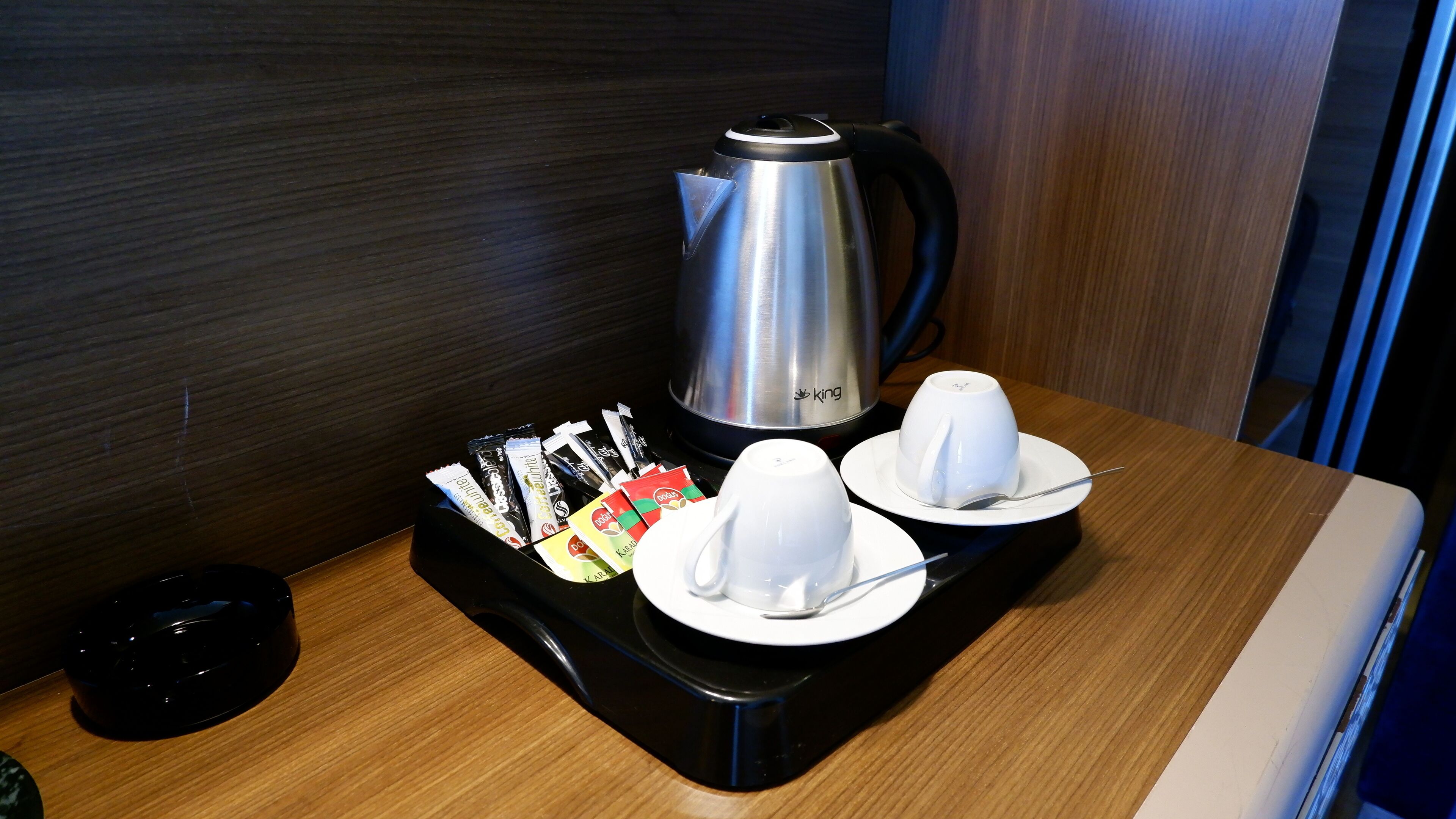 A coffee station with a coffee maker, cups, and tea packets on a tray.