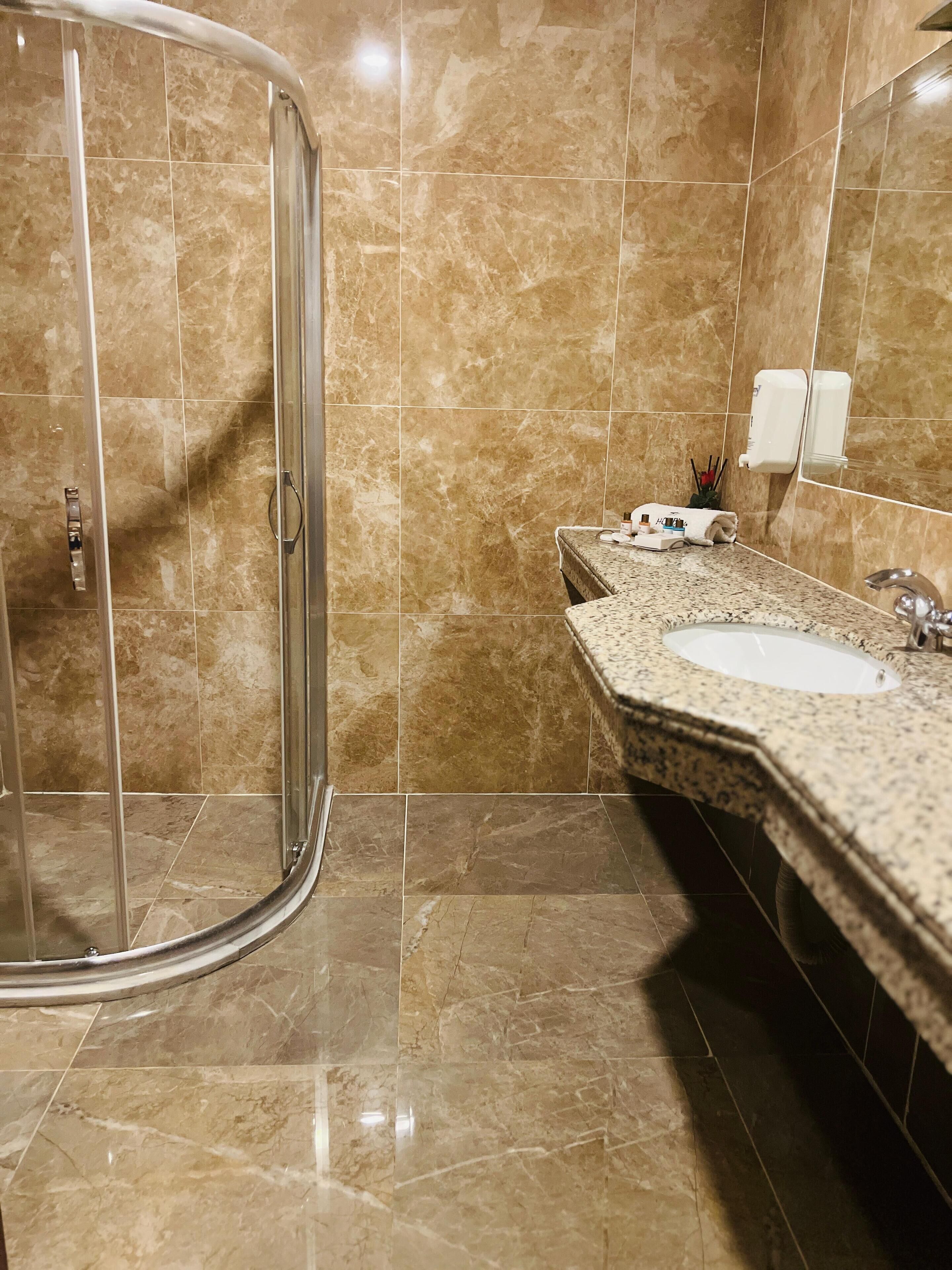 Un baño con cabina de ducha de vidrio, un lavamanos con encimera de mármol y dispensador de jabón en la pared.