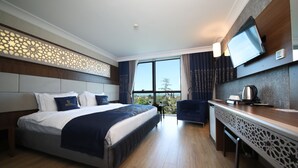 Habitación de hotel con una cama grande, un escritorio, una silla, un televisor y vistas al exterior.