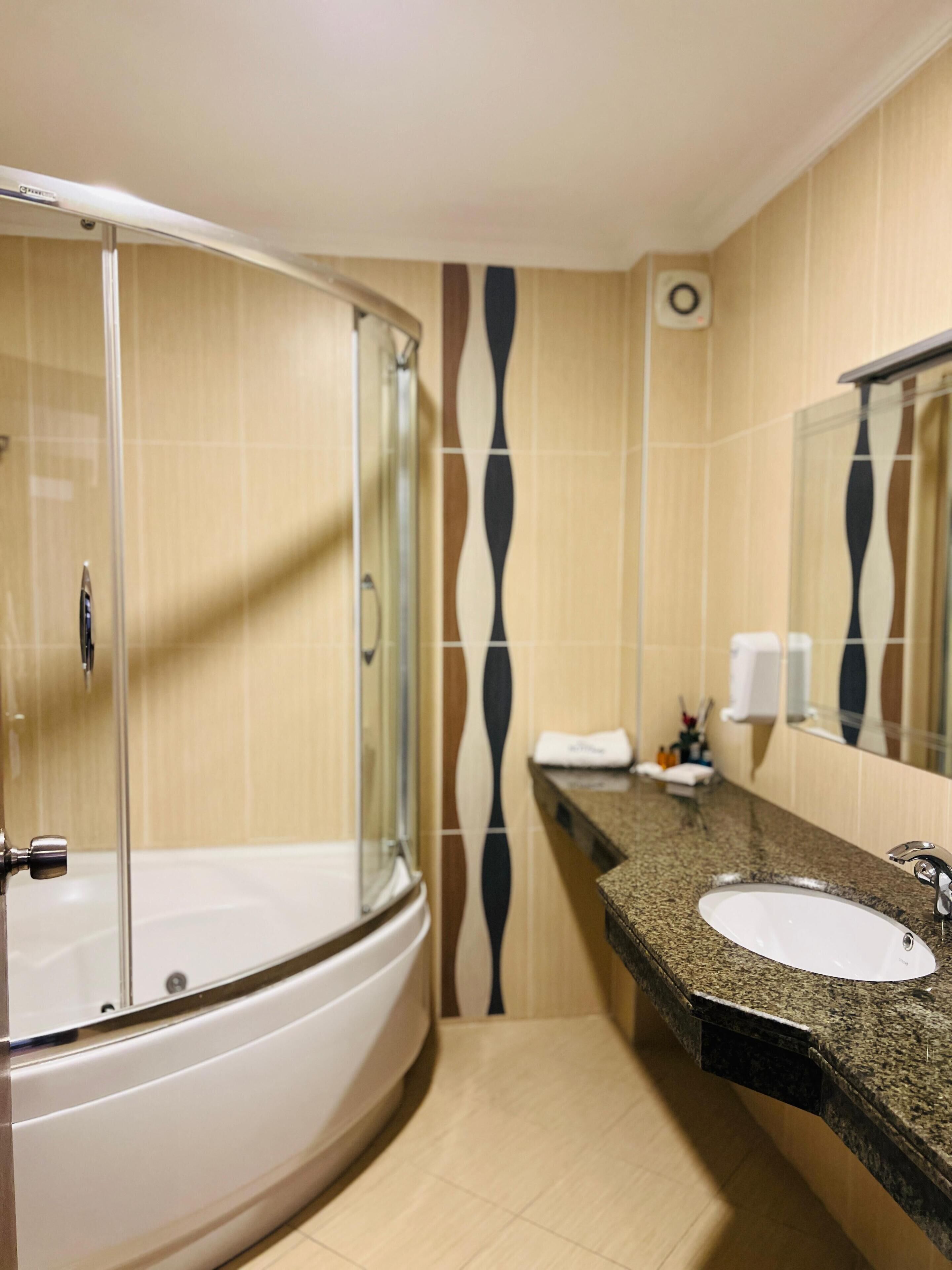 Un baño con ducha de vidrio, lavamanos con encimera de granito y espejo sobre el lavamanos.