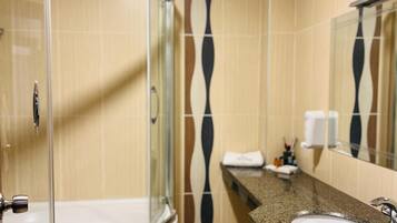 Un baño con ducha de vidrio, lavamanos con encimera de granito y espejo sobre el lavamanos.