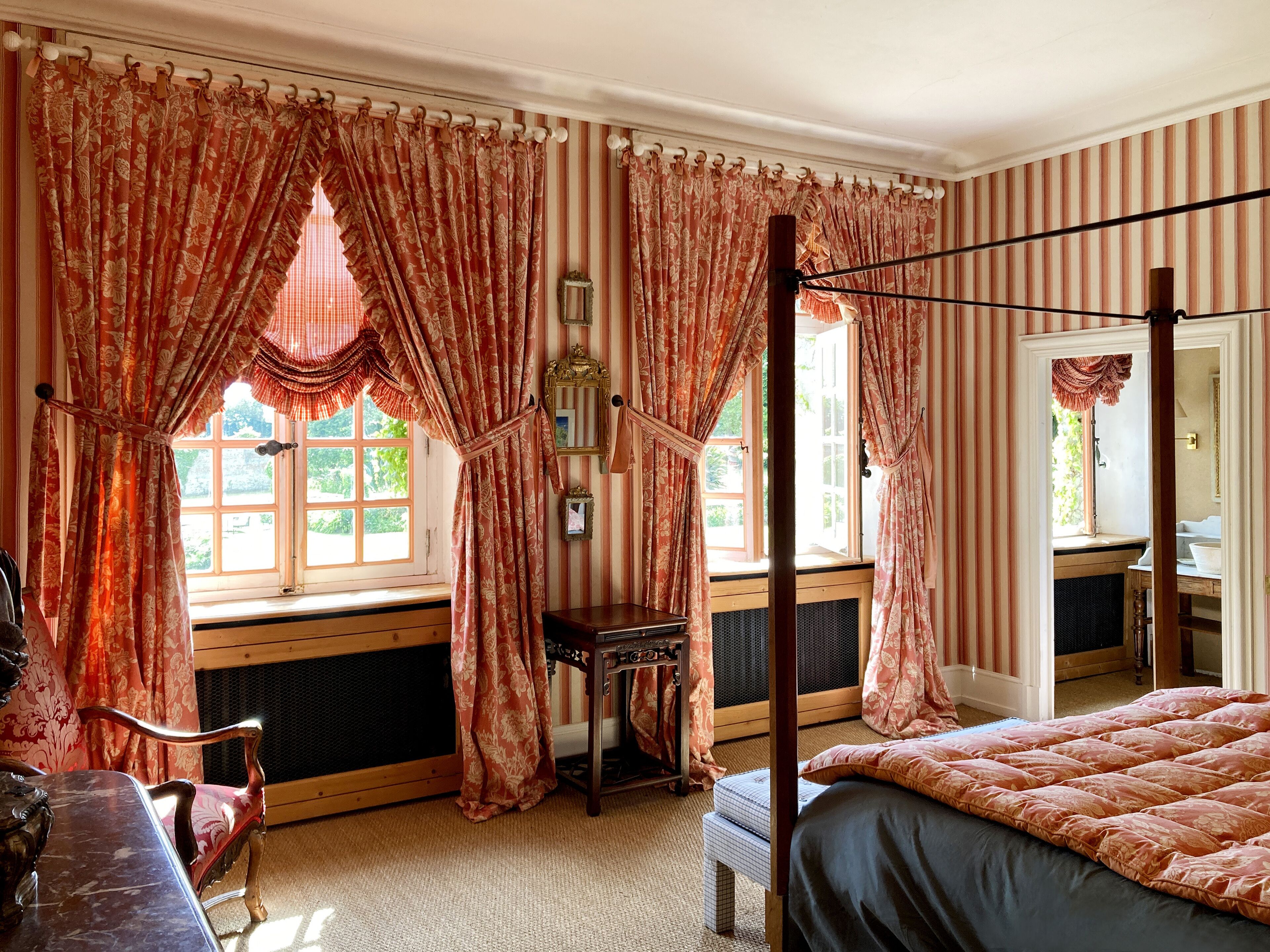 Une chambre avec un lit à baldaquin, une chaise en bois, une petite table et une fenêtre avec des rideaux.