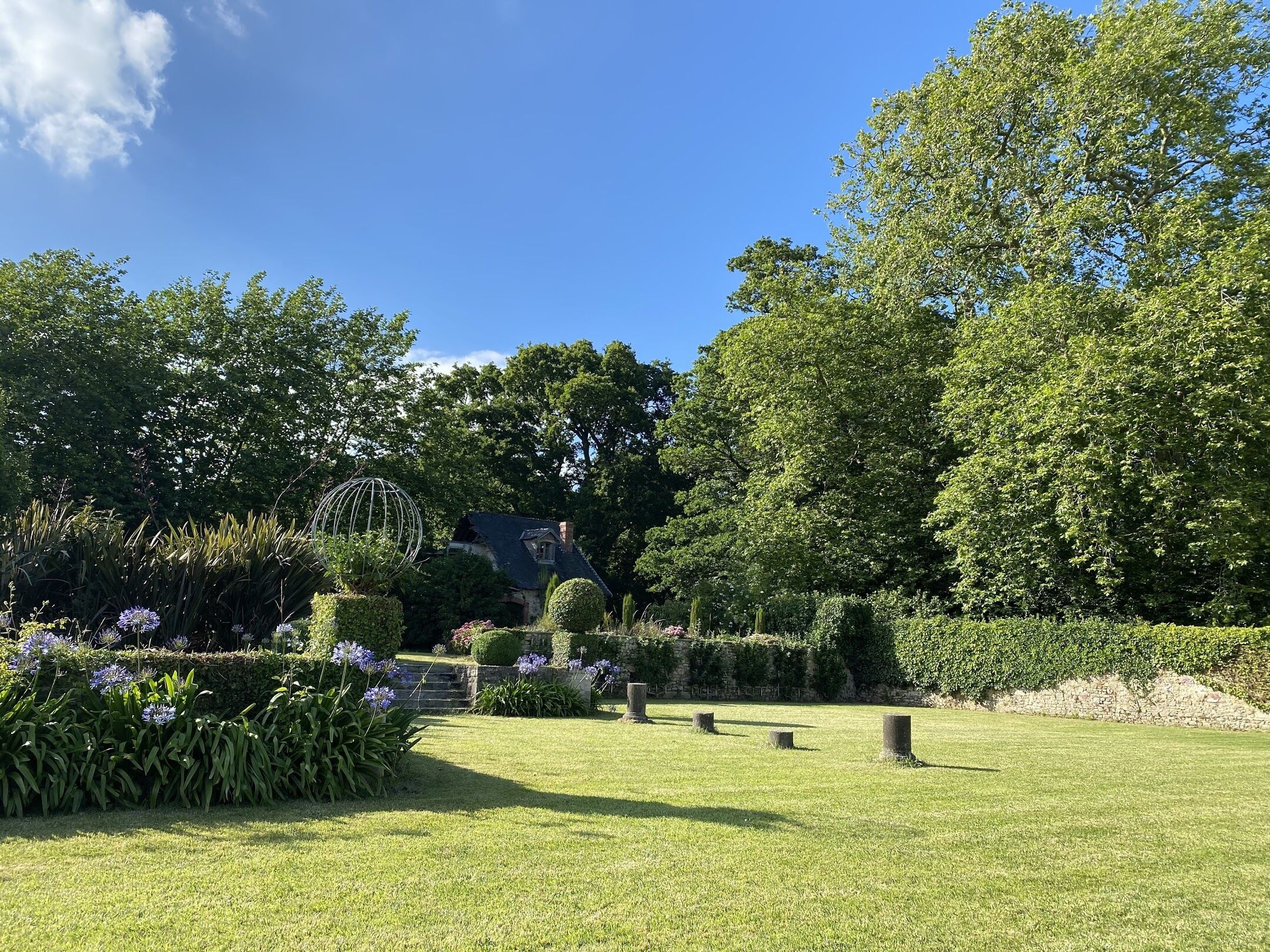 A well-maintained garden with a variety of plants and a spherical metal sculpture.