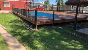 Ein umzäunter Garten mit Pool, einem roten Haus und einem Gebäude mit Strohdach.