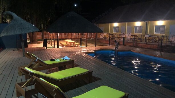 Ein Poolbereich mit Holzliegen und Sonnenschirmen, einem Pool und einem Gebäude mit mehreren Fenstern im Hintergrund.