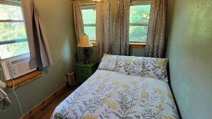 A bedroom with a bed, a ceiling fan, a window with curtains, and a lamp on a nightstand.
