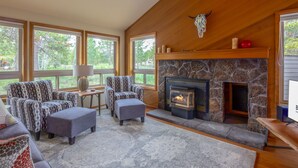 A cozy living room with a stone fireplace, patterned armchairs, and a large window overlooking greenery. - YANK01 - Cozy Home, Gas Fireplace, Dog Friendly (Sunriver)