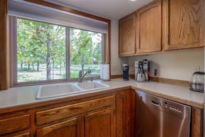 Enjoy a serene view from the large window in this kitchen, featuring a double sink, coffee maker, and dishwasher.