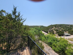 A wooden deck with a metal railing overlooking a hilly landscape with dense greenery and a small building. - Turner Falls Cabins #2 in Turner Falls Park (Davis)