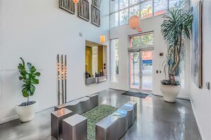 A modern lobby with a central seating area, large windows, and potted plants.