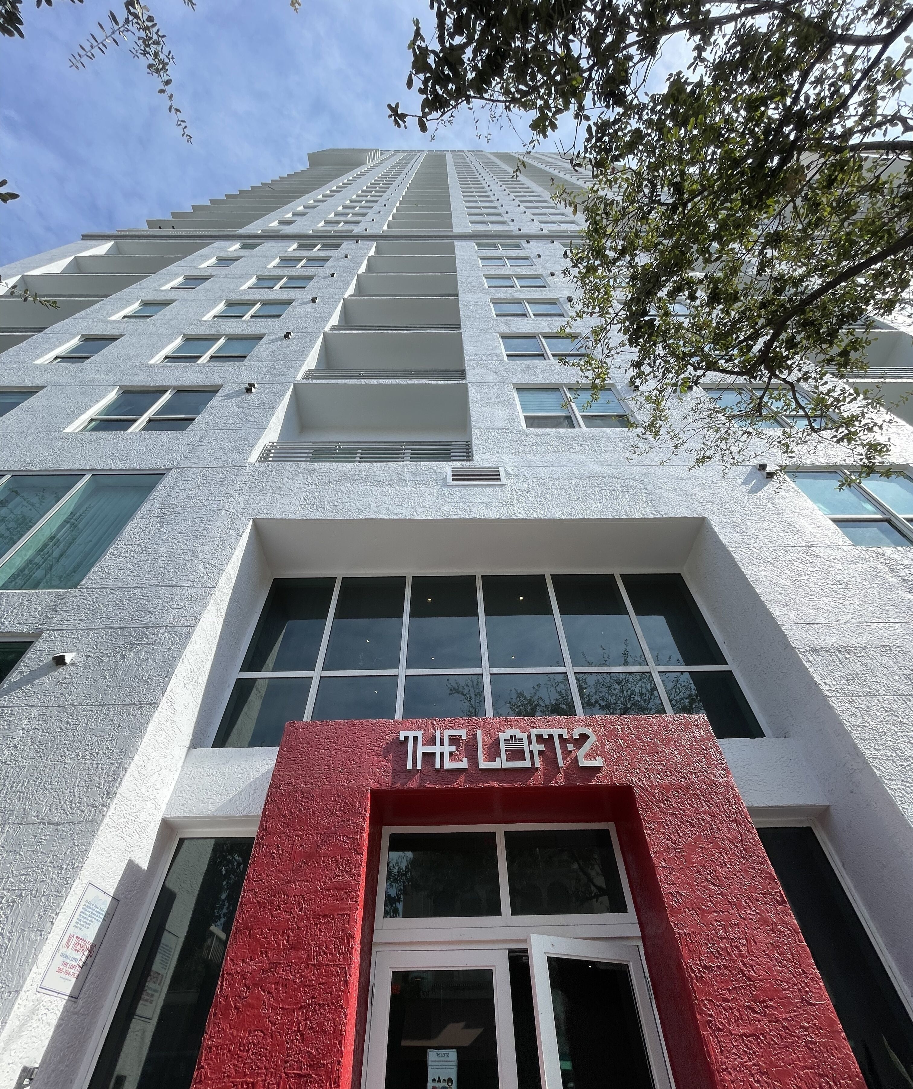 A high-rise building with a prominent red entrance labeled "THE LOFT2".