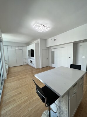 A modern kitchen with a central island, wooden flooring, white cabinetry, and a ceiling light fixture.