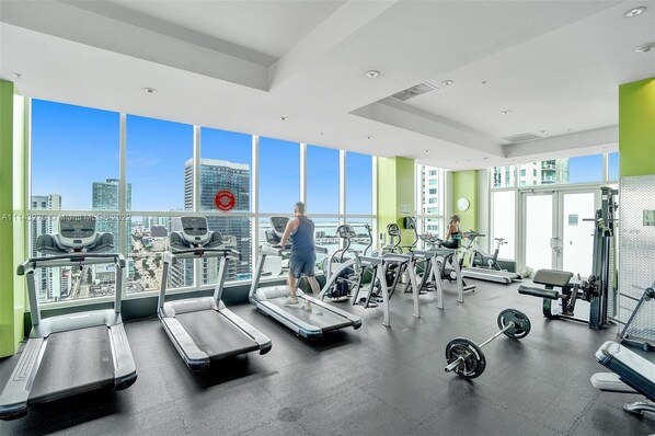 A gym with treadmills, weights, and exercise equipment, large windows with a city view.