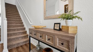 Una escalera con peldaños alfombrados, una consola de madera con cajones, un espejo y una planta en maceta.